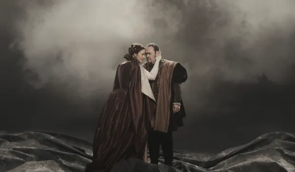 Woman playing Lady Macbeth presses her forehead to forehead of man playing Macbeth on smoky stage at the Met